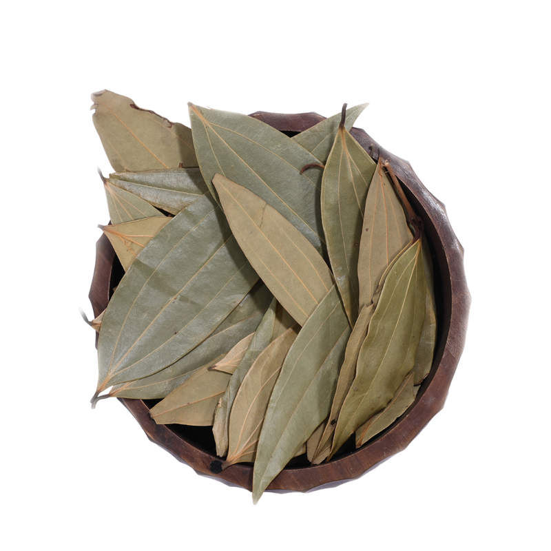 A bowl of dried bay leaves on a wooden kitchen counter, with a House of Rasda product label beside it
