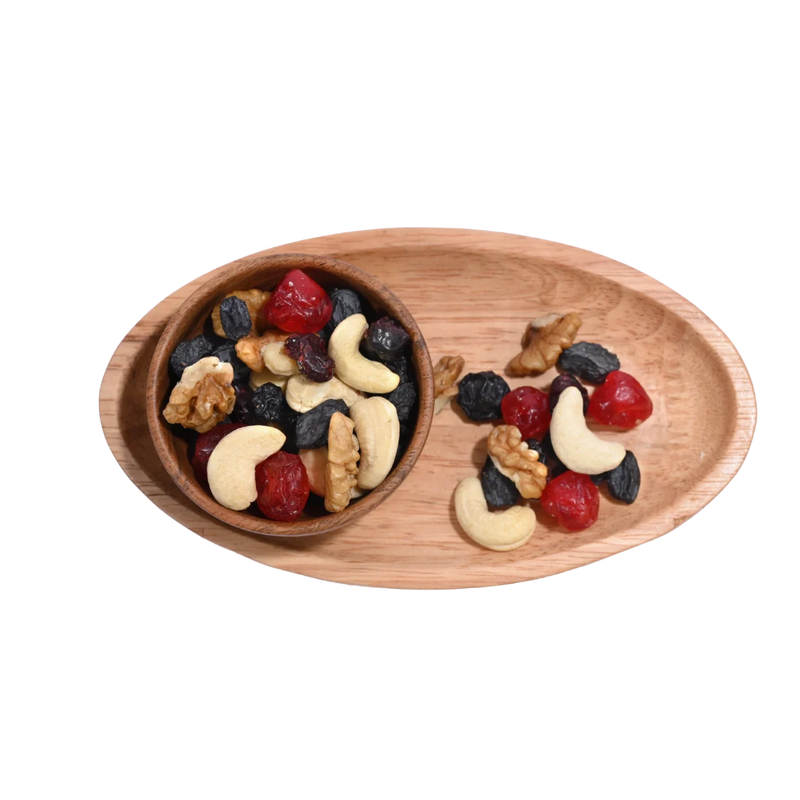 Berry Nutty Trail Mix Wooden platter with a bowl of mixed nuts and dried fruits on a white background