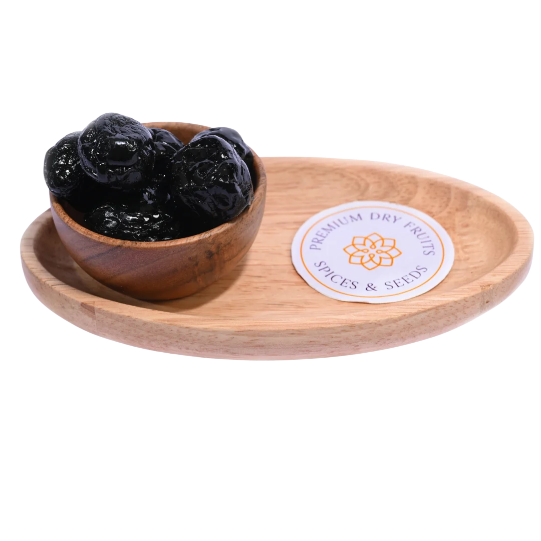 Black Plums Dehydrated in a rustic wooden bowl placed on a wooden surface.