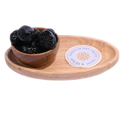 Black Plums Dehydrated in a rustic wooden bowl placed on a wooden surface.
