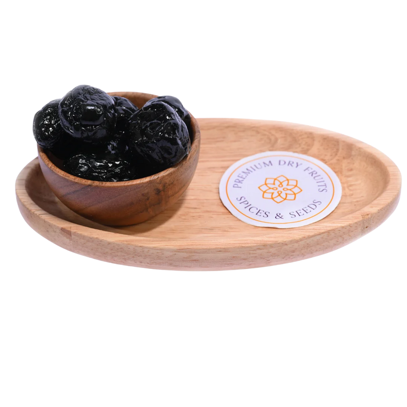 Black Plums Dehydrated in a rustic wooden bowl placed on a wooden surface.