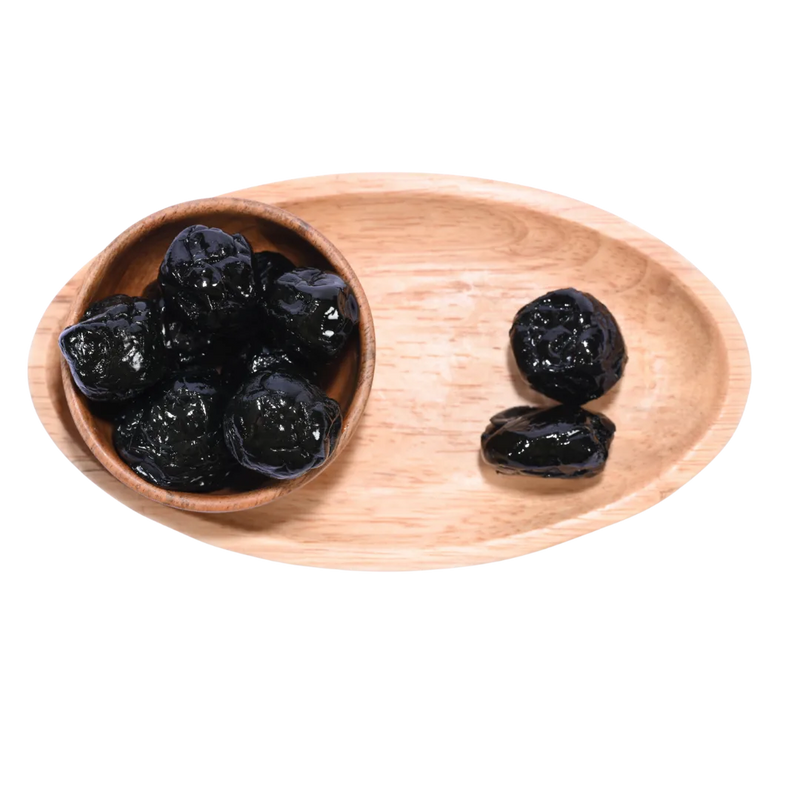 Black Plums Dehydrated neatly displayed in a natural wooden bowl under soft lighting