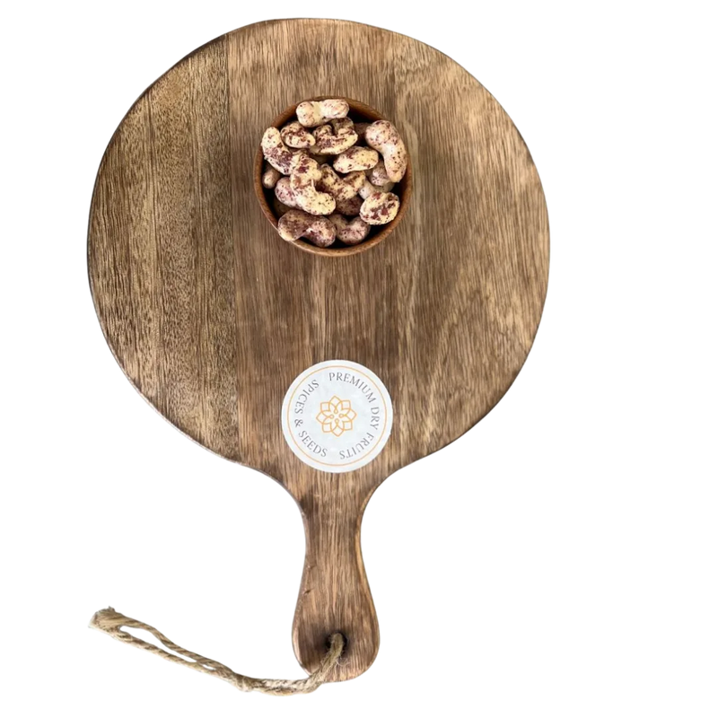 Wooden serving board with a handle and a small bowl of Cashew Nuts Rose Petal on a white background