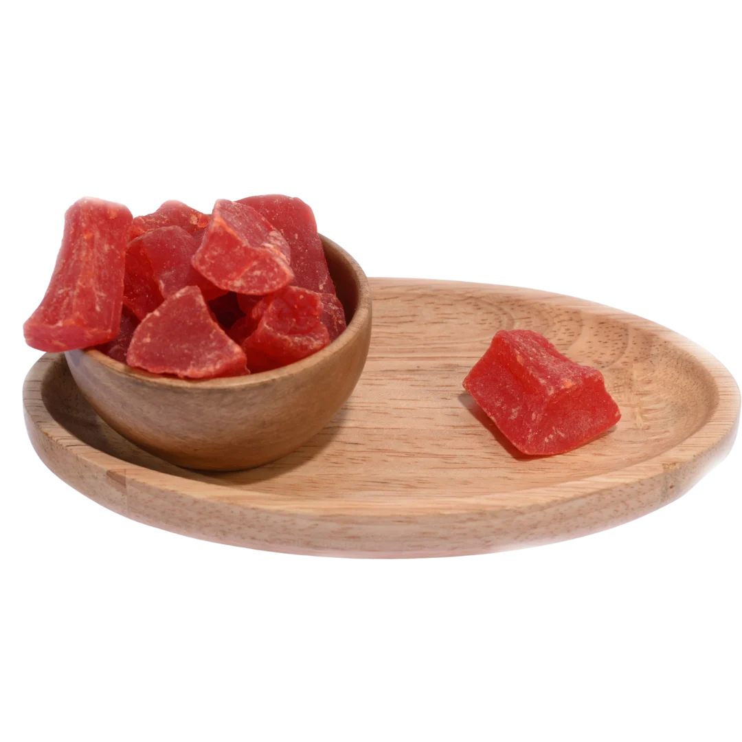 Wooden bowl filled with dried papaya cubes placed on a wooden table.