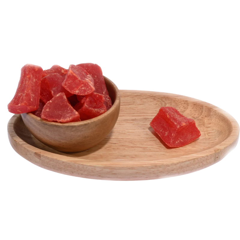Wooden bowl filled with dried papaya cubes placed on a wooden table.