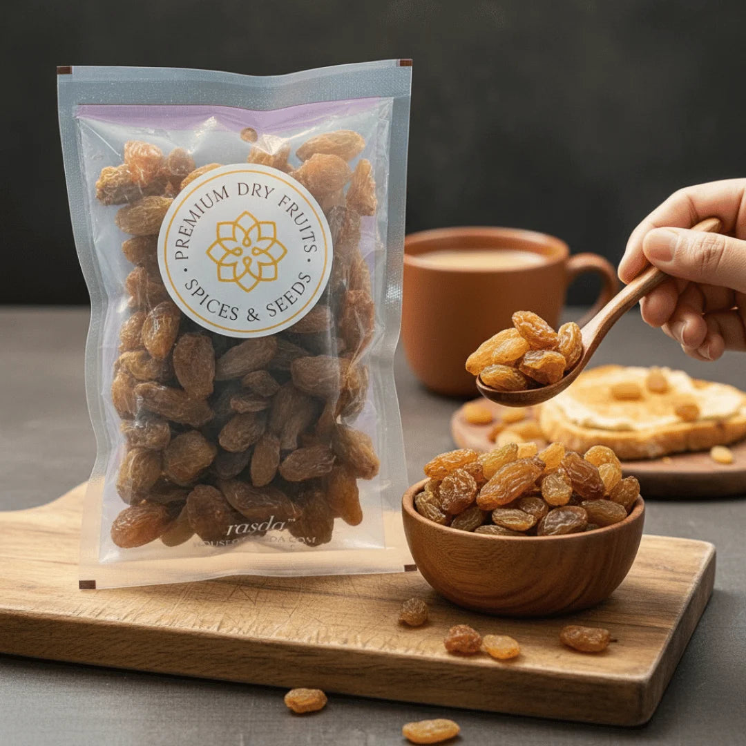 Packaged Munakka Raisins Premium with a spoonful of raisins, a bowl of raisins, and a cup in the background on a wooden board.