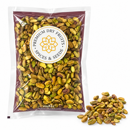 Pistachio pieces in a pouch with pieces scattered beside it on a white background