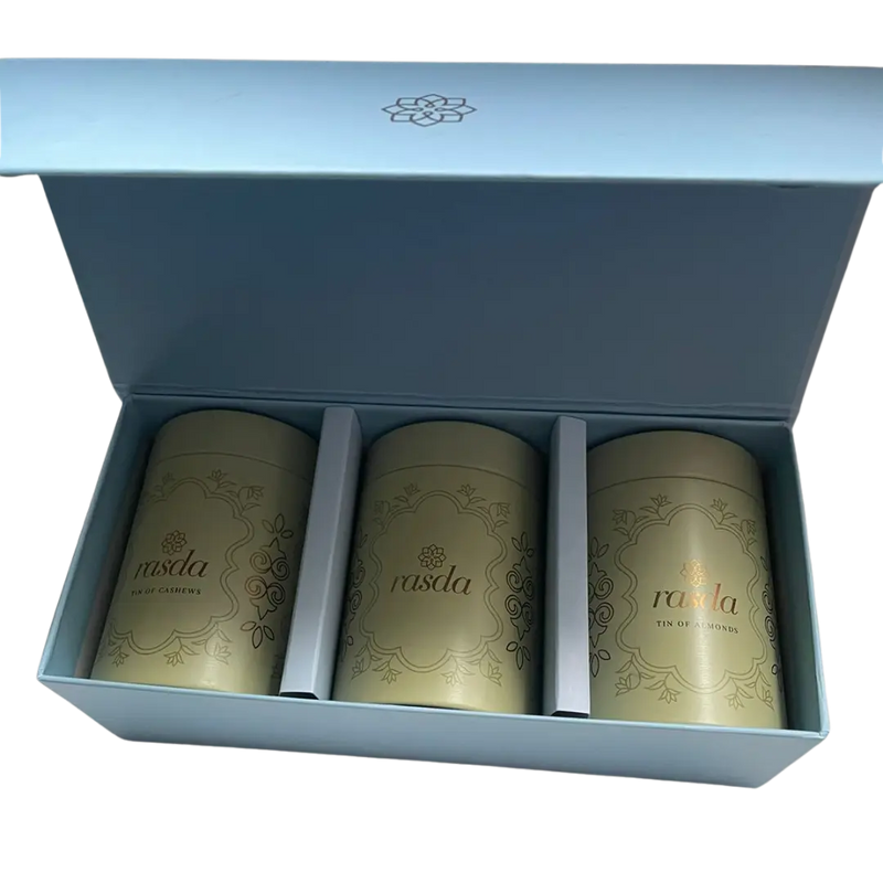 Three gold tea canisters in a blue box with branding. Premium nuts and dry fruits packed in designer airtight tins for festive gifting
