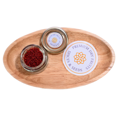 A glass jars with Saffron or Kesar on a wooden tray, featuring 'Premium Dry Fruits & Spices' branding.