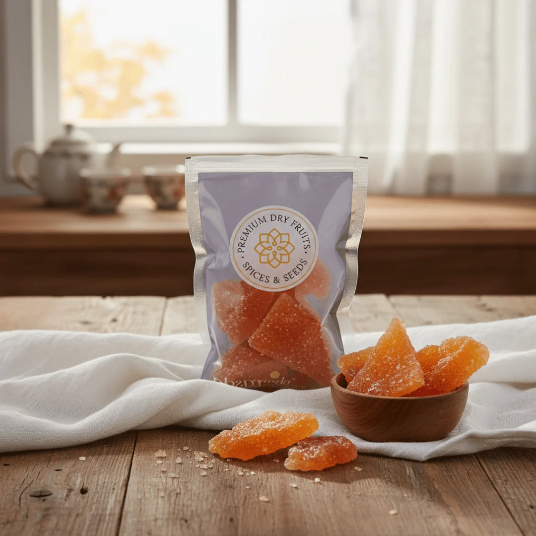Packaged Orange Sugar Candy on a wooden table with a bowl of sugar candy and a teapot in the background.