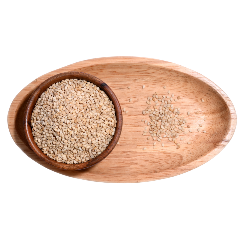 Wooden Bowl filled with white sesame seeds, some seeds spilling out onto a wooden table