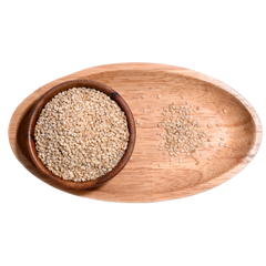 Wooden Bowl filled with white sesame seeds, some seeds spilling out onto a wooden table