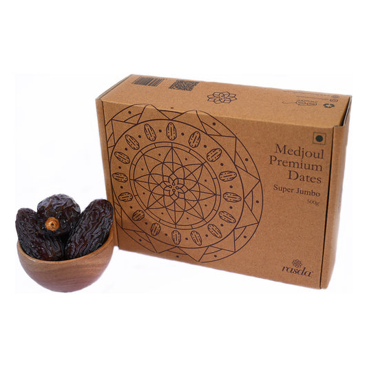 Super Jumbo Medjool dates 500g gift box beside a wooden bowl of the dates on a white background