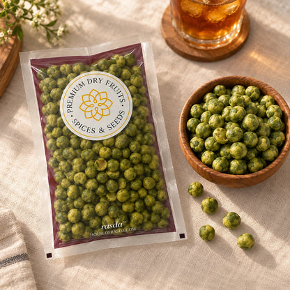Wasabi coated green peas in a pouch on a linen surface with a wooden bowl of peas and a glass of iced tea